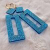 Boucles d'oreilles (fermoirs dormeuses plaqué or 24k) en résine bleue à paillettes composée d'un petit carré et d'un rectangle plus long.