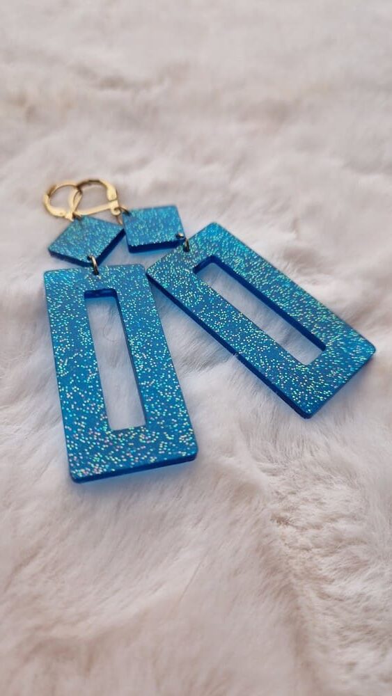 Boucles d'oreilles (fermoirs dormeuses plaqué or 24k) en résine bleue à paillettes composée d'un petit carré et d'un rectangle plus long.