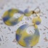 Boucles d'oreilles (fermoirs dormeuse plaqué or 24k) en résine colorée (mauve, jaune, blanc) composée d'un petit rond et d'un ovale plus large.